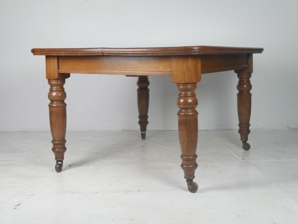 A 19th-century oak extending dining table featuring turned baluster legs set on brass castors with an inserted extension leaf. View VII
