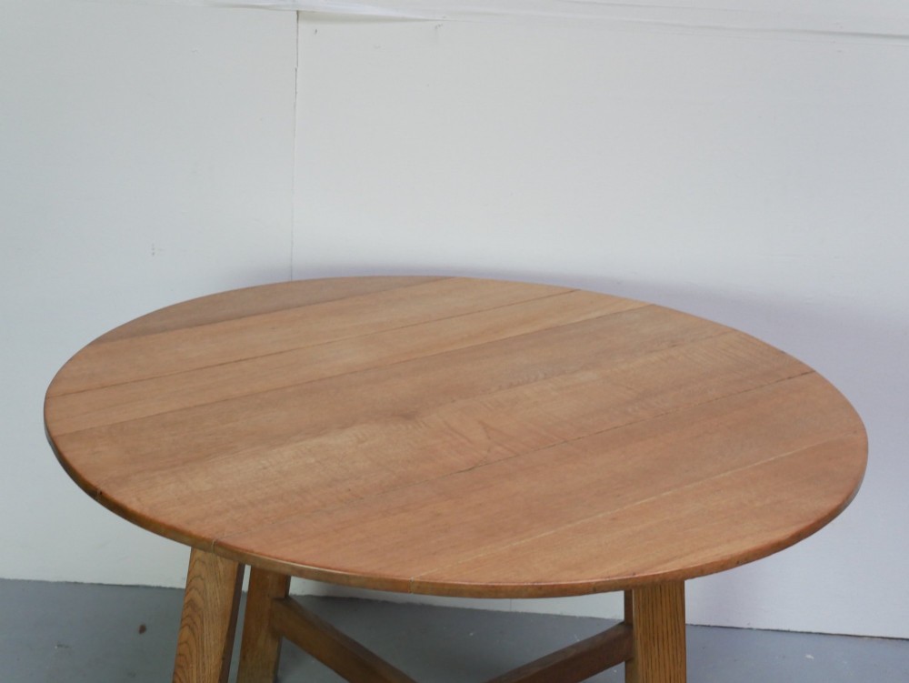 A circular solid oak centre table featuring splayed square legs connected by a central cross-stretcher. View II