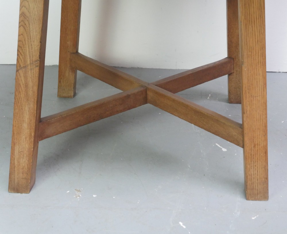 A circular solid oak centre table featuring splayed square legs connected by a central cross-stretcher. View III