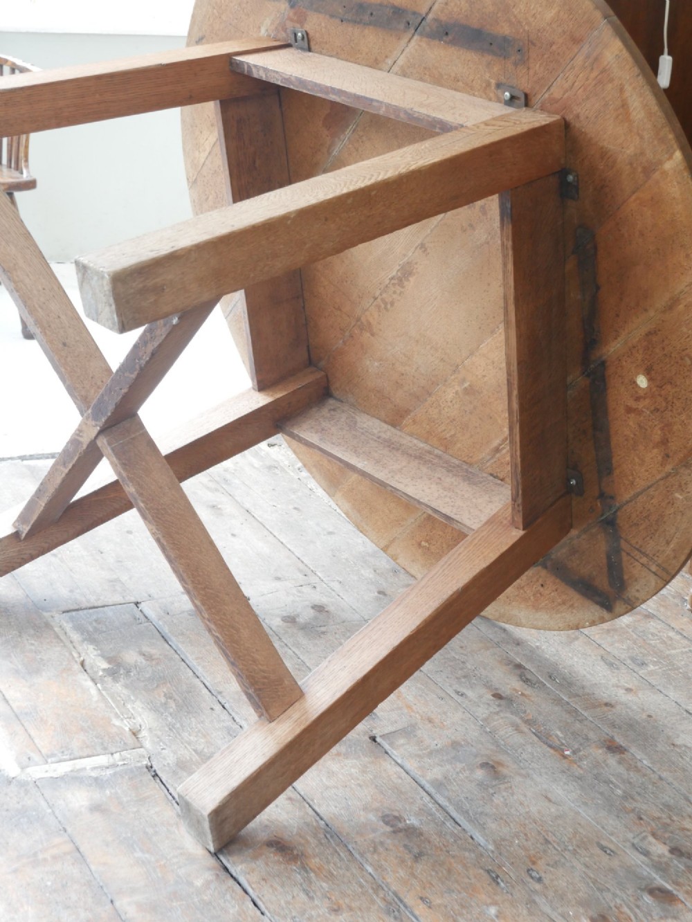 A circular solid oak centre table featuring splayed square legs connected by a central cross-stretcher. View VIII