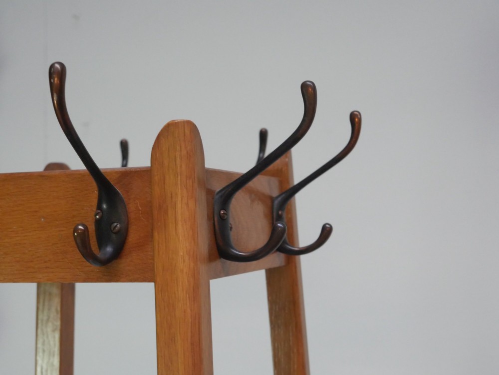 A tall tapered solid oak coat and umbrella stand featuring dark metal hooks around the top and a square metal drip tray set into the wooden base. View II
