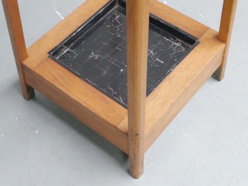 A tall tapered solid oak coat and umbrella stand featuring dark metal hooks around the top and a square metal drip tray set into the wooden base. View V
