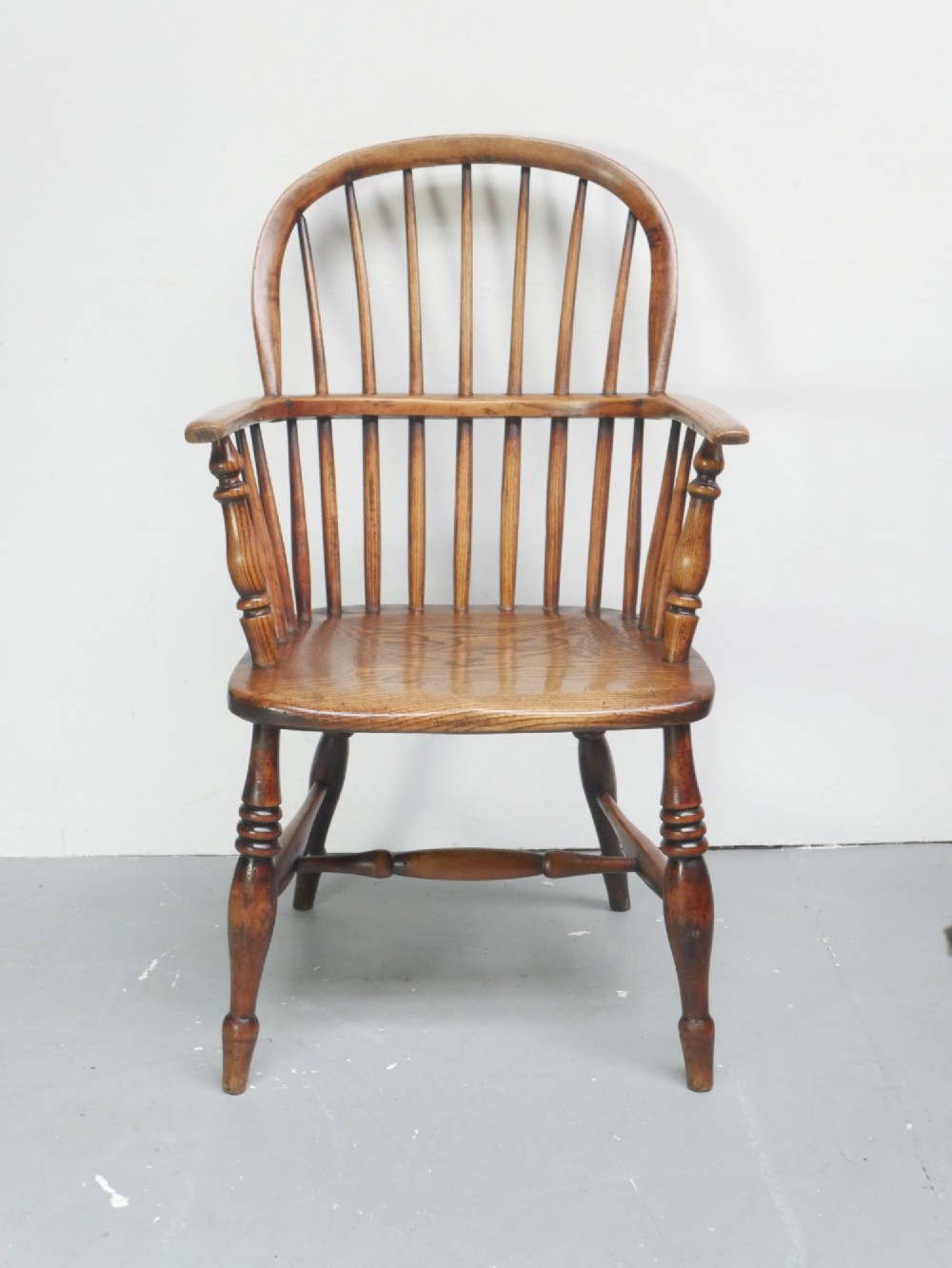 A warm brown wooden Scottish Windsor armchair featuring a hoop back with vertical spindles, shaped saddle seat, and turned legs.