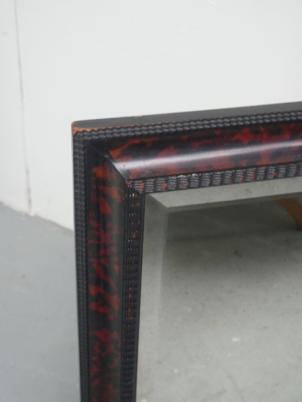 A rectangular wall mirror with a dark red and black mottled faux tortoiseshell frame featuring beaded inner moulding. View II