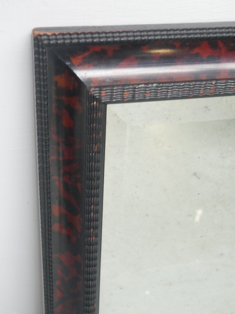 A rectangular wall mirror with a dark red and black mottled faux tortoiseshell frame featuring beaded inner moulding. View VII