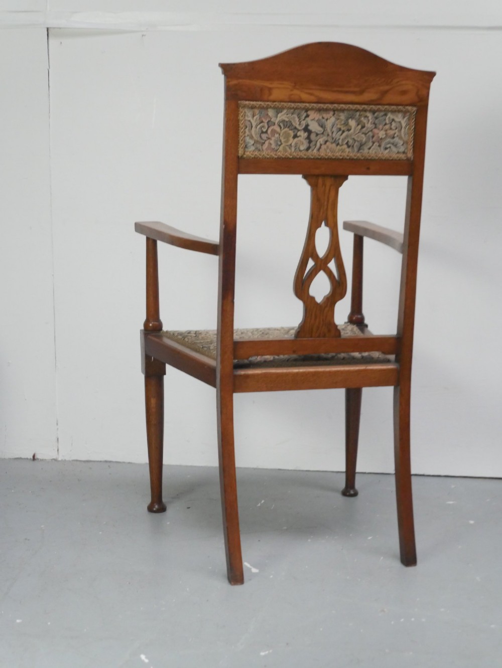 An antique oak armchair featuring a carved top rail, tapestry fabric back panel and seat, and a pierced decorative back splat. View IV