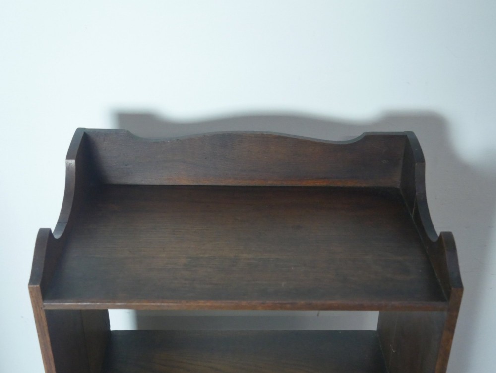 A narrow dark oak open bookcase with four fixed shelves, a shaped gallery top upstand, and a solid plinth base. View II