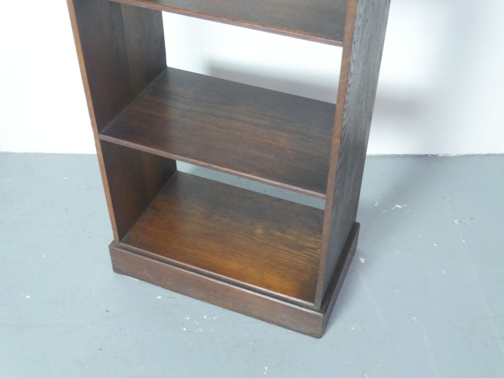 A narrow dark oak open bookcase with four fixed shelves, a shaped gallery top upstand, and a solid plinth base. View IV