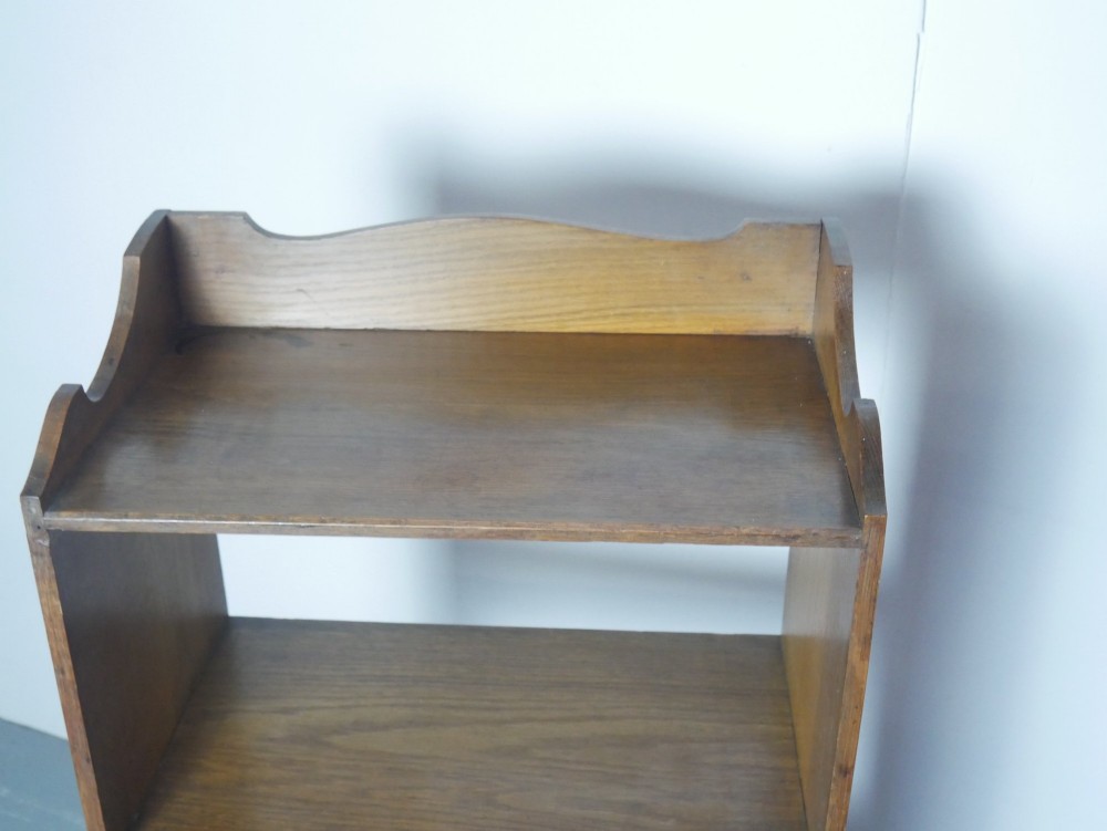 A tall, narrow freestanding open oak bookcase with four shelves, a plinth base, and a shaped top gallery. View II