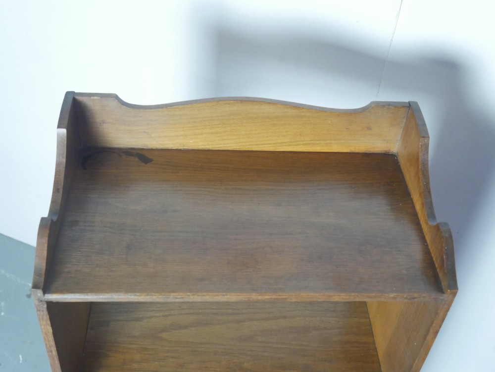 A tall, narrow freestanding open oak bookcase with four shelves, a plinth base, and a shaped top gallery. View VII