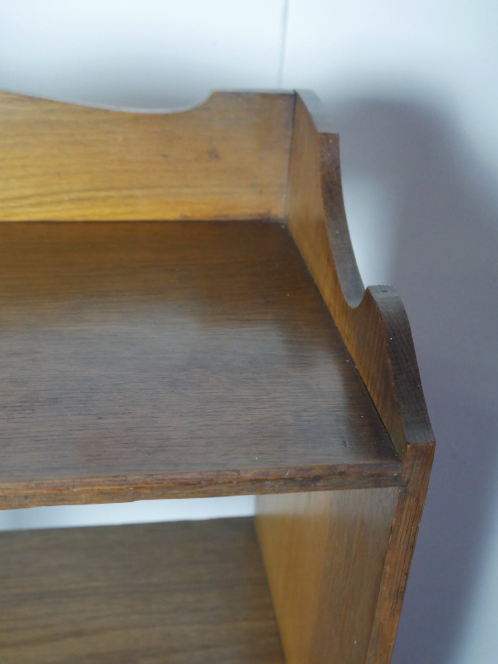 A tall, narrow freestanding open oak bookcase with four shelves, a plinth base, and a shaped top gallery. View VIII