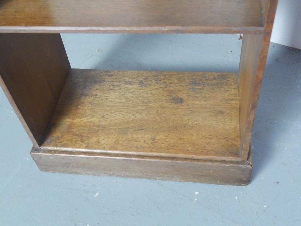 A tall, narrow freestanding open oak bookcase with four shelves, a plinth base, and a shaped top gallery. View IX