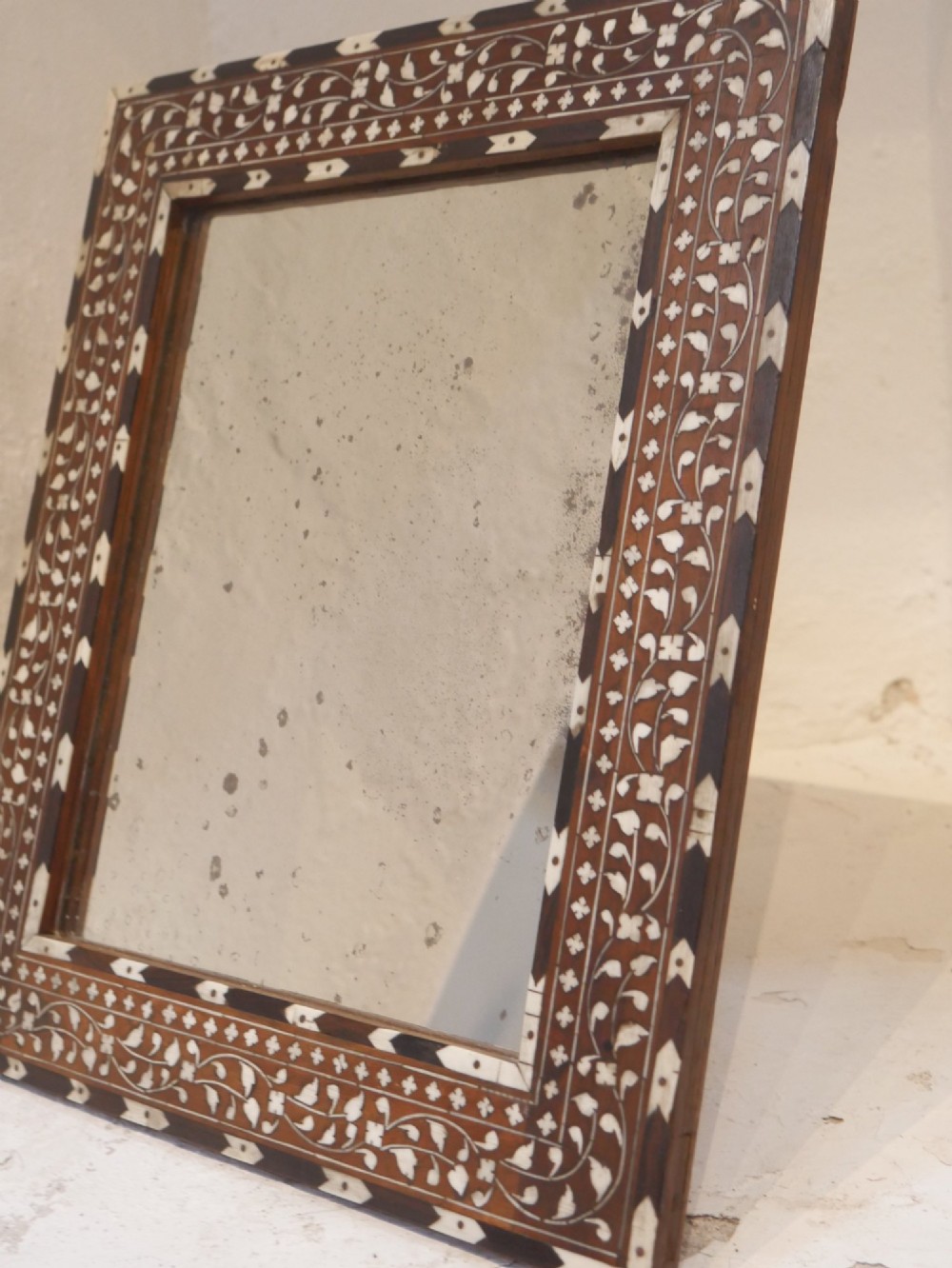 A nineteenth-century rectangular wooden mirror frame with intricate white floral bone inlay patterns surrounding foxed mirror glass. View V