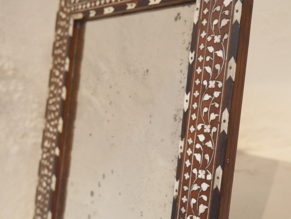 A nineteenth-century rectangular wooden mirror frame with intricate white floral bone inlay patterns surrounding foxed mirror glass. View VII