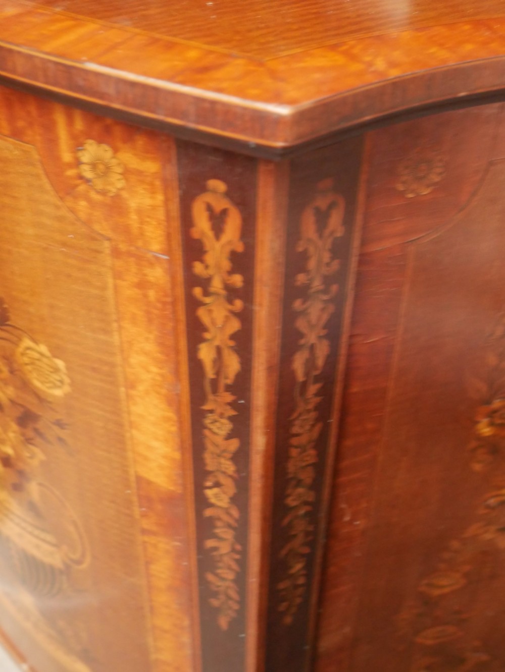 An antique mahogany display cabinet featuring marquetry urn inlays on lower doors, curved bowfront glass doors, glass shelves, and a swan-neck pediment. View XI