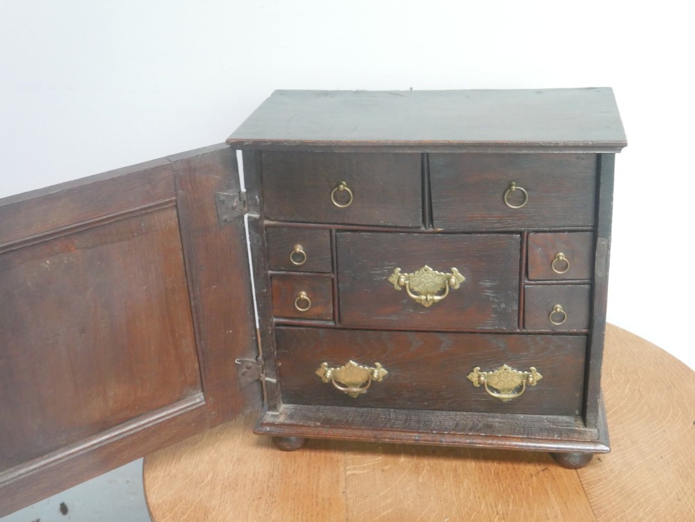 An 18th-century dark oak spice cupboard with a single fielded panel door, brass escutcheon, and bun feet. View II