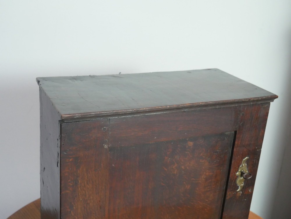 An 18th-century dark oak spice cupboard with a single fielded panel door, brass escutcheon, and bun feet. View VI