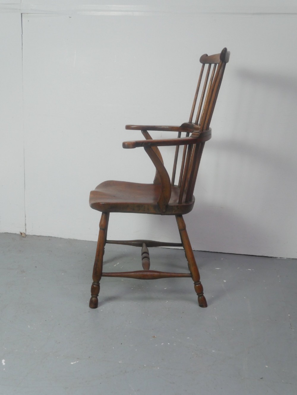 A mid-19th-century warm brown wooden Windsor armchair featuring a double-tier spindle back, carved saddle seat, curved armrests, and turned legs. View II