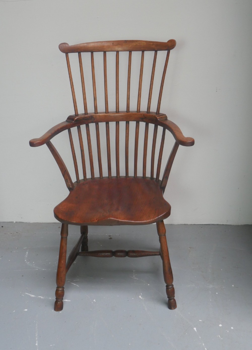 A mid-19th-century warm brown wooden Windsor armchair featuring a double-tier spindle back, carved saddle seat, curved armrests, and turned legs. View XV