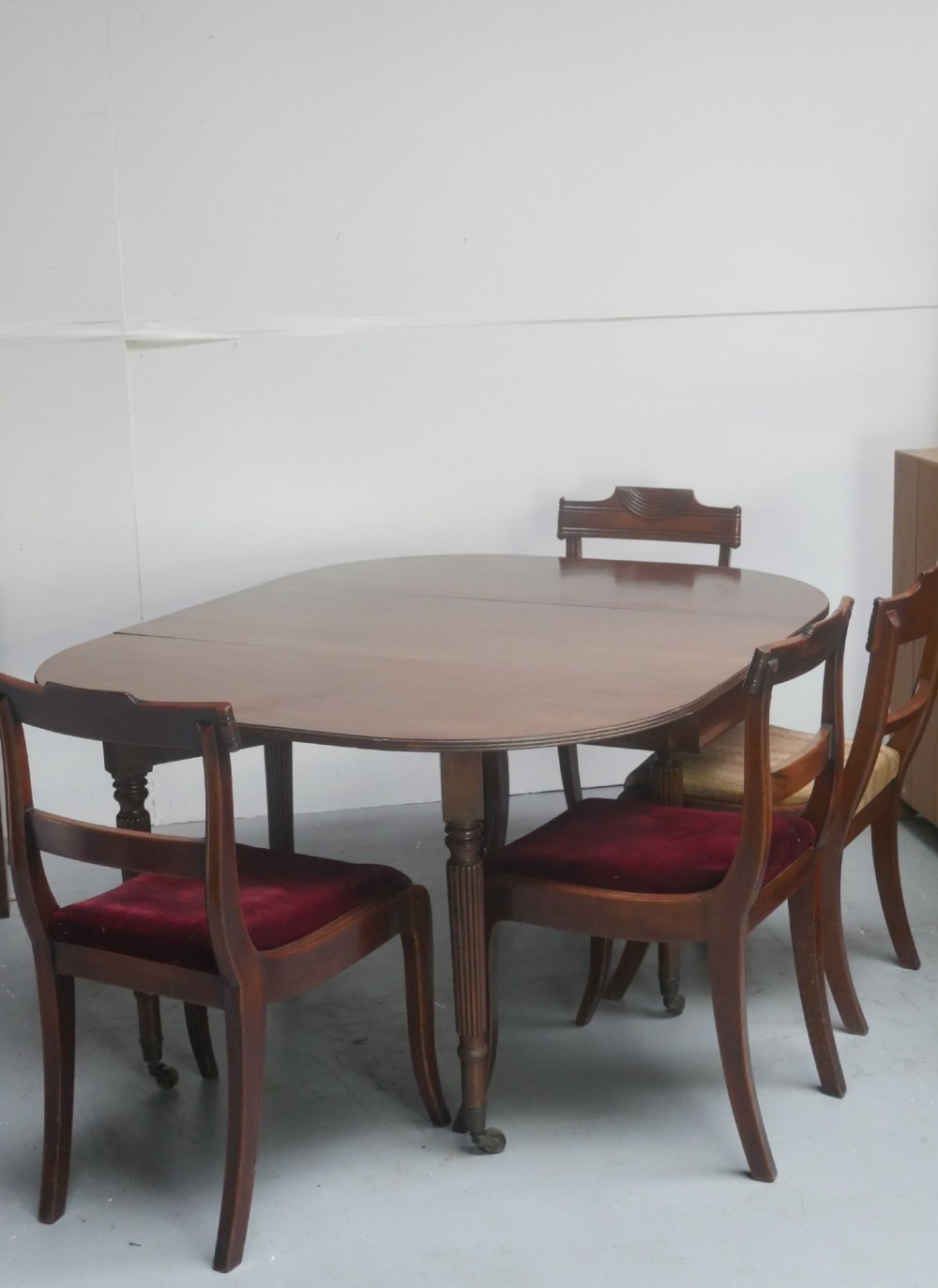 An antique mahogany drop-leaf dining table featuring reeded turned legs set on brass castors, displayed with both side leaves lowered. View X