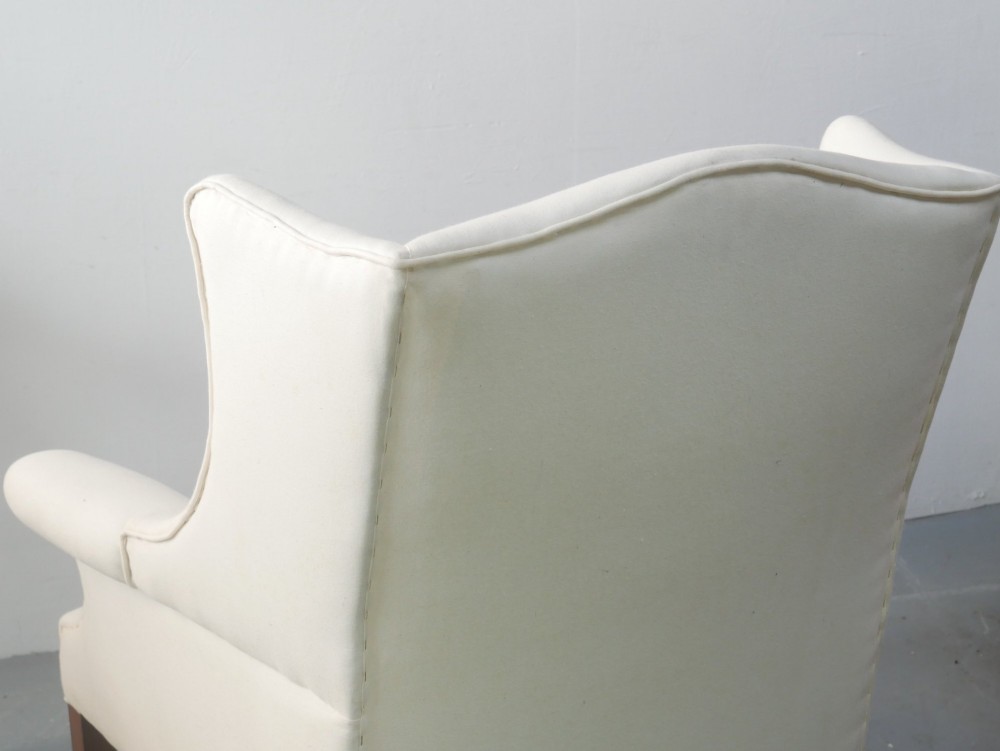 A pair of Edwardian wingback armchairs upholstered in cream fabric with square mahogany legs on brass castors. View V