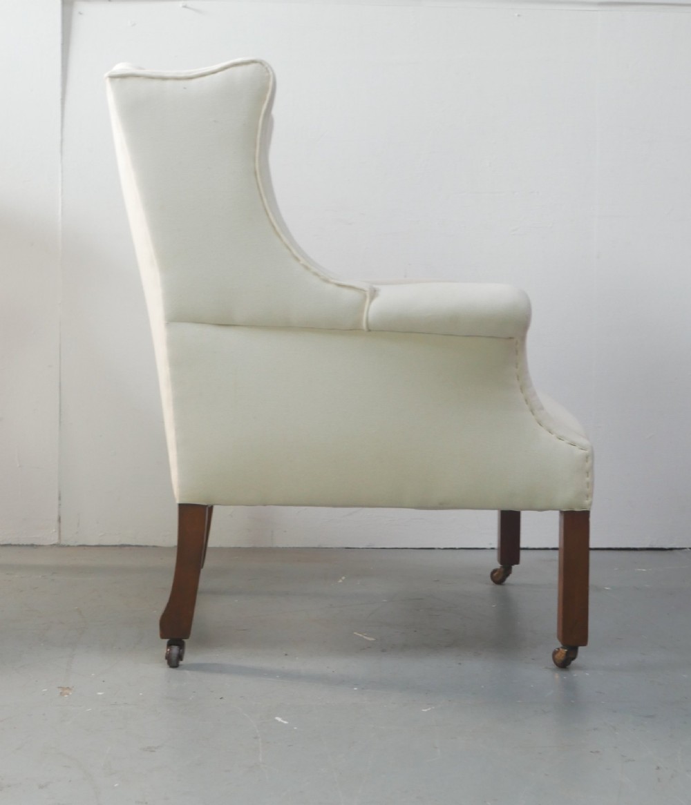 A pair of Edwardian wingback armchairs upholstered in cream fabric with square mahogany legs on brass castors. View VI