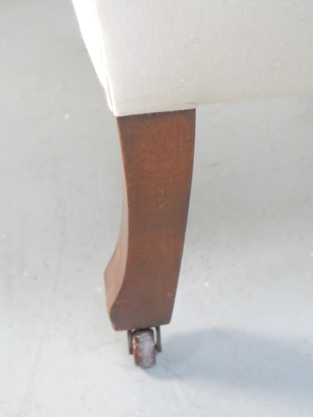 A pair of Edwardian wingback armchairs upholstered in cream fabric with square mahogany legs on brass castors. View VII