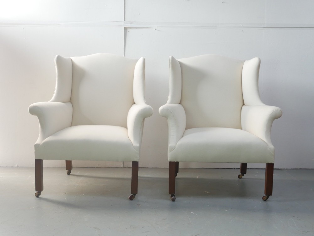 A pair of Edwardian wingback armchairs upholstered in cream fabric with square mahogany legs on brass castors. View VIII