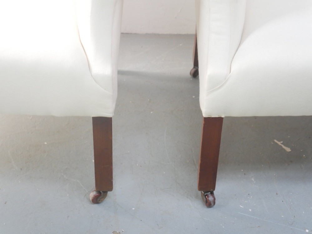 A pair of Edwardian wingback armchairs upholstered in cream fabric with square mahogany legs on brass castors. View IX