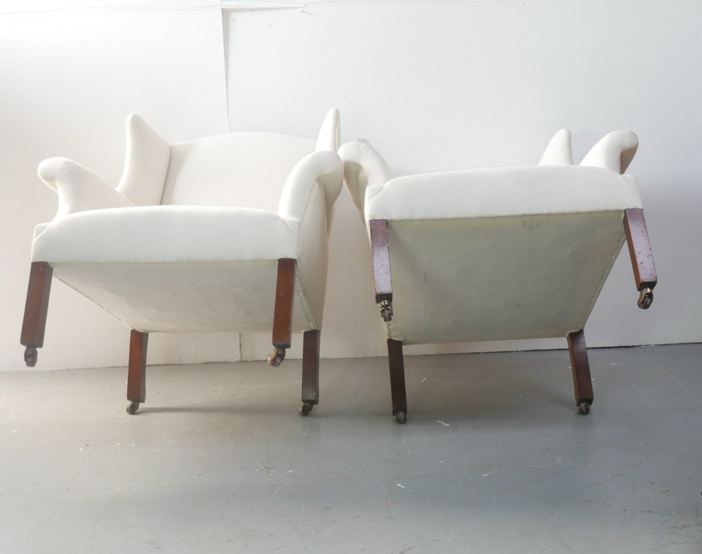 A pair of Edwardian wingback armchairs upholstered in cream fabric with square mahogany legs on brass castors. View XI