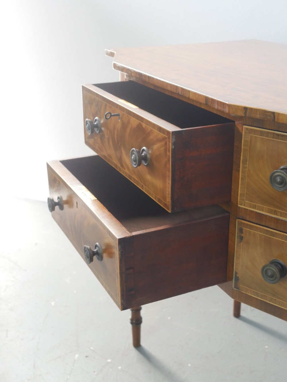 A small Regency mahogany side cabinet featuring flame mahogany drawer fronts, brass knob handles, inlaid borders, and slender turned legs. View V