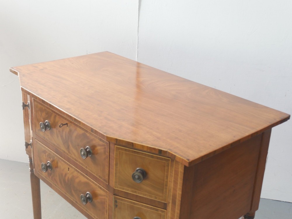 A small Regency mahogany side cabinet featuring flame mahogany drawer fronts, brass knob handles, inlaid borders, and slender turned legs. View VI