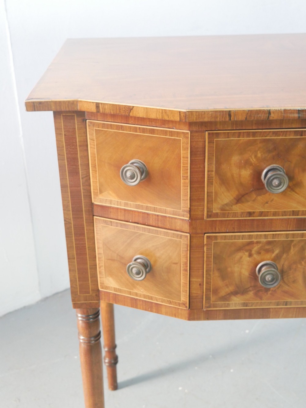 A small Regency mahogany side cabinet featuring flame mahogany drawer fronts, brass knob handles, inlaid borders, and slender turned legs. View VII