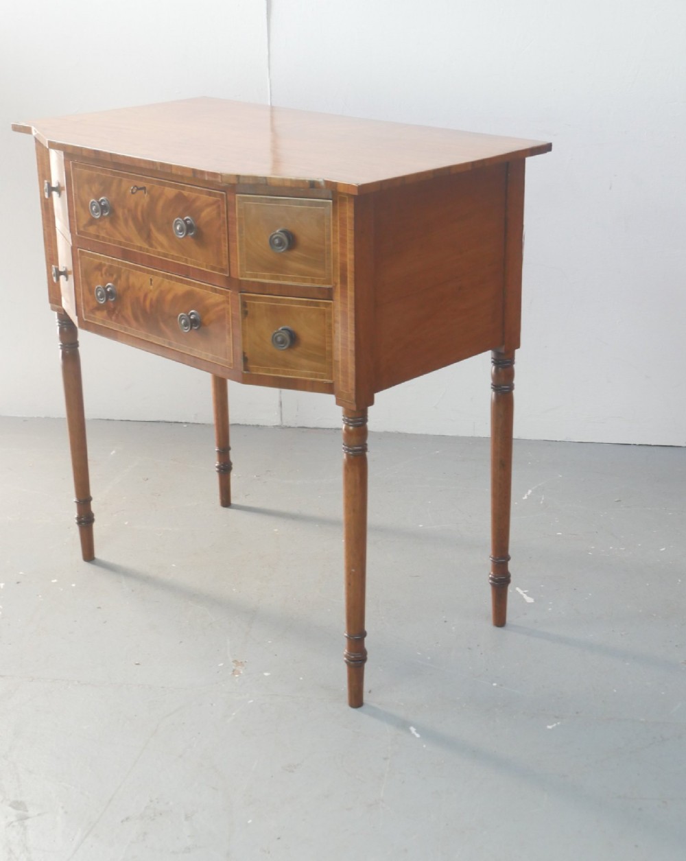 A small Regency mahogany side cabinet featuring flame mahogany drawer fronts, brass knob handles, inlaid borders, and slender turned legs. View VIII