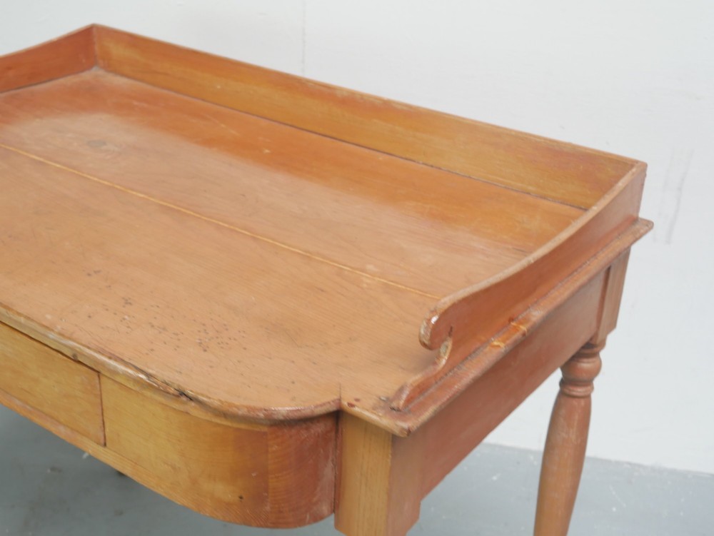 A Regency warm pine writing table featuring turned legs, a single central drawer with a brass knob, and a raised gallery upstand along the top. View VI