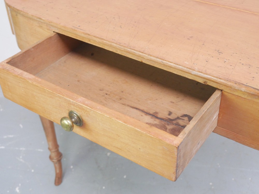 A Regency warm pine writing table featuring turned legs, a single central drawer with a brass knob, and a raised gallery upstand along the top. View VII