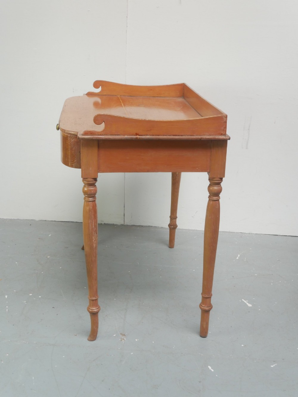 A Regency warm pine writing table featuring turned legs, a single central drawer with a brass knob, and a raised gallery upstand along the top. View VIII