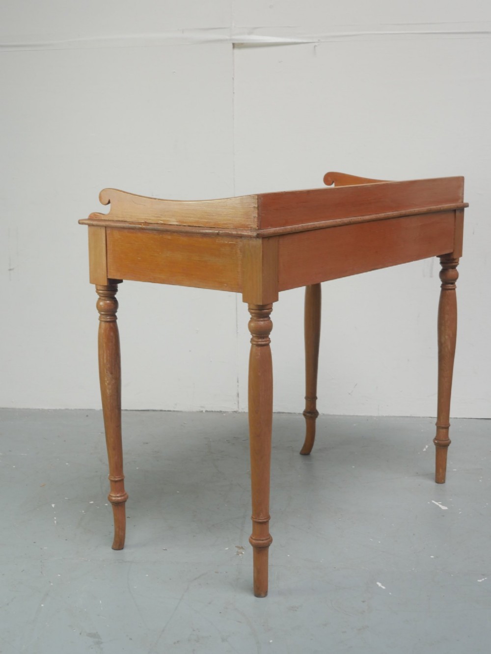 A Regency warm pine writing table featuring turned legs, a single central drawer with a brass knob, and a raised gallery upstand along the top. View IX