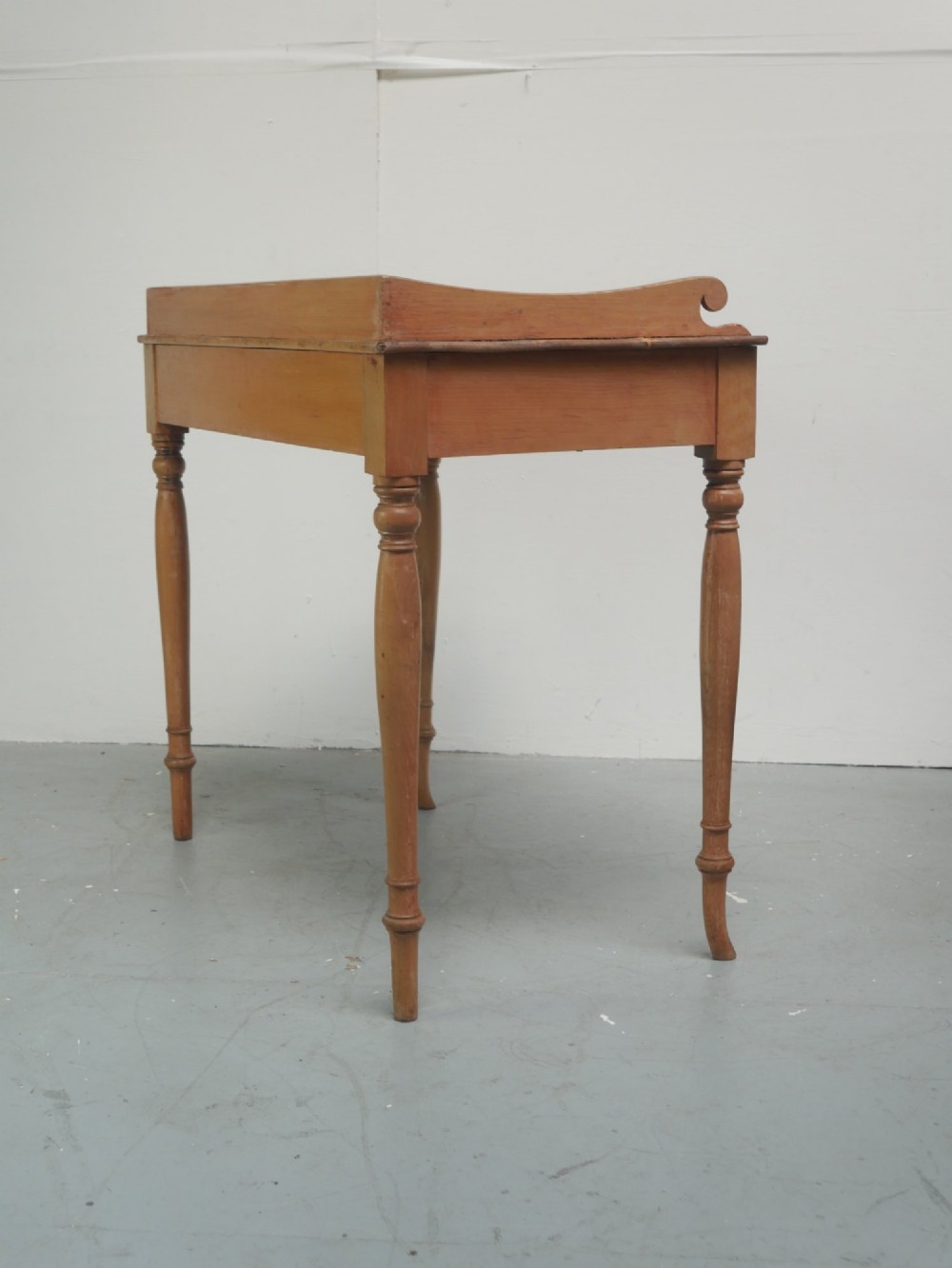 A Regency warm pine writing table featuring turned legs, a single central drawer with a brass knob, and a raised gallery upstand along the top. View X