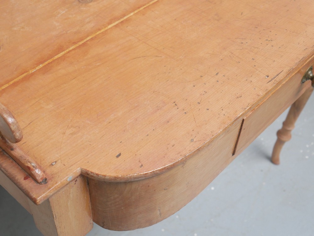 A Regency warm pine writing table featuring turned legs, a single central drawer with a brass knob, and a raised gallery upstand along the top. View XII