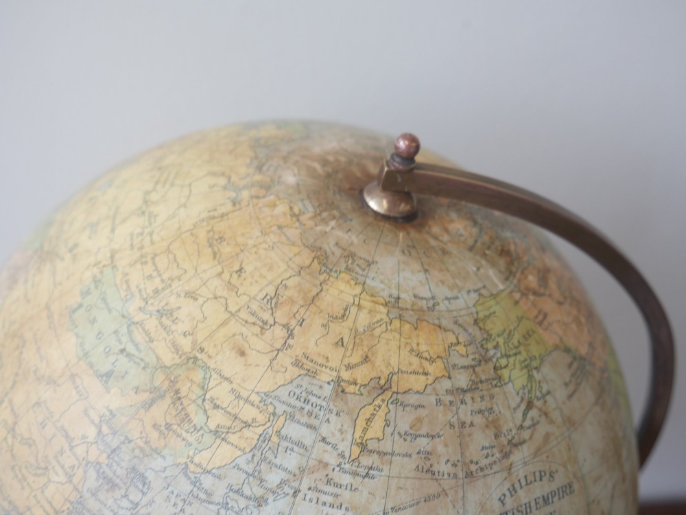An antique terrestrial desk globe titled Philips British Empire Globe featuring cream paper gores mounted on a brass semi-meridian arm and an ebonised turned wooden base. View II