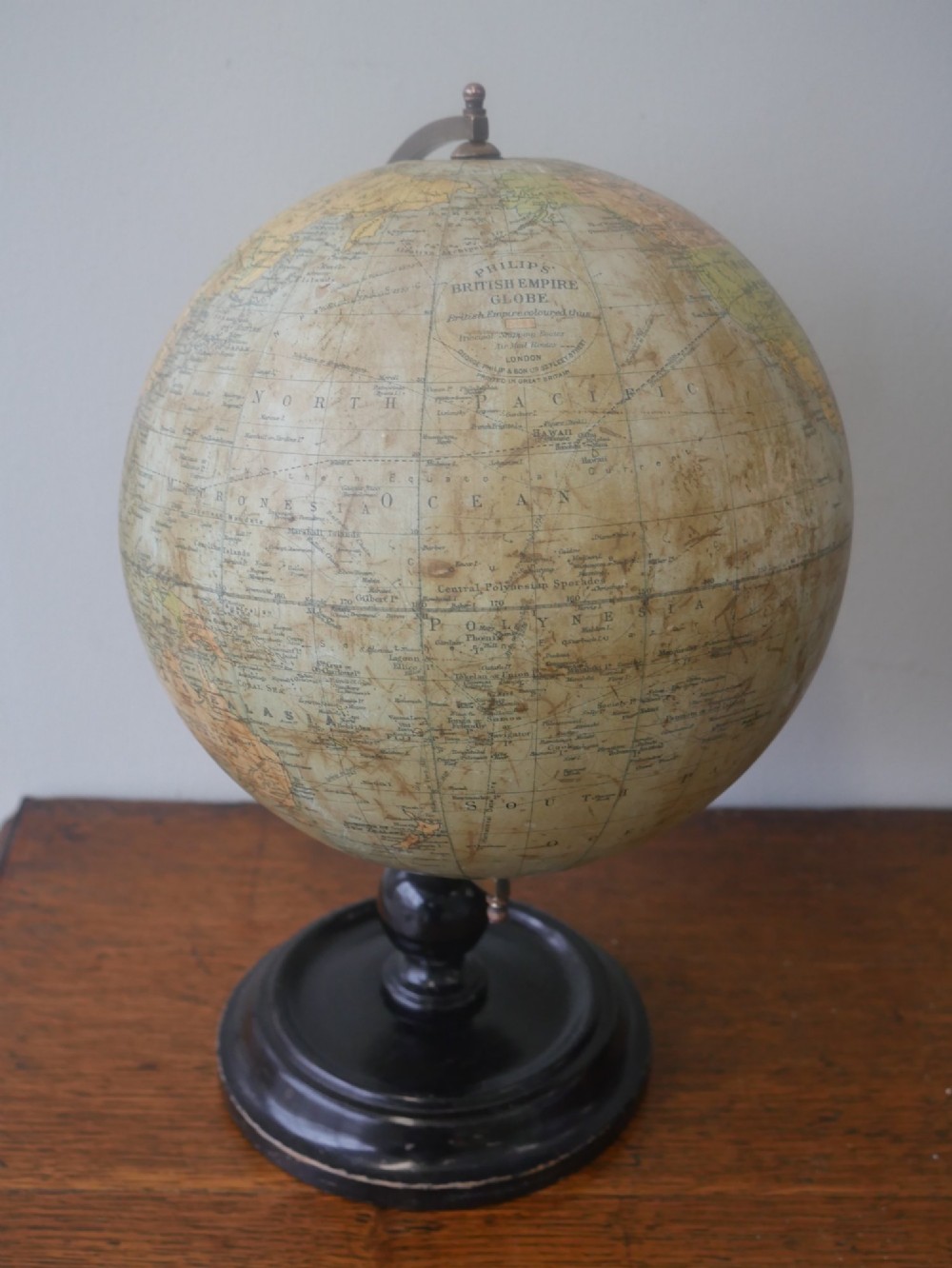 An antique terrestrial desk globe titled Philips British Empire Globe featuring cream paper gores mounted on a brass semi-meridian arm and an ebonised turned wooden base. View VIII