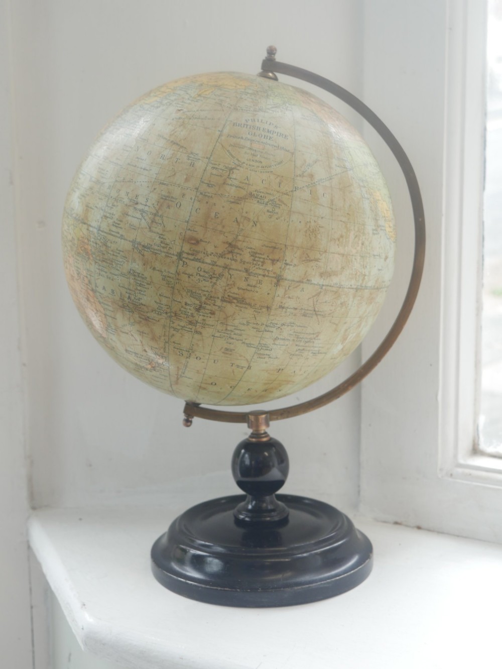 An antique terrestrial desk globe titled Philips British Empire Globe featuring cream paper gores mounted on a brass semi-meridian arm and an ebonised turned wooden base. View XII