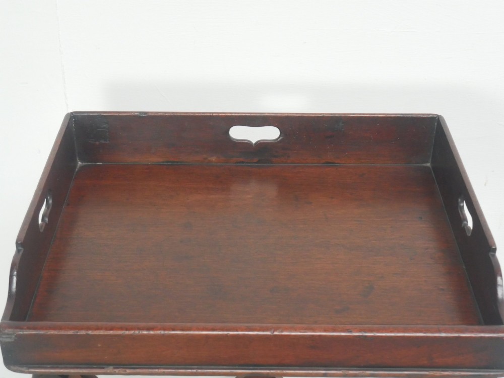 A dark mahogany butlers tray with integrated hand cutout handles resting on a matching folding x-frame stand. View II