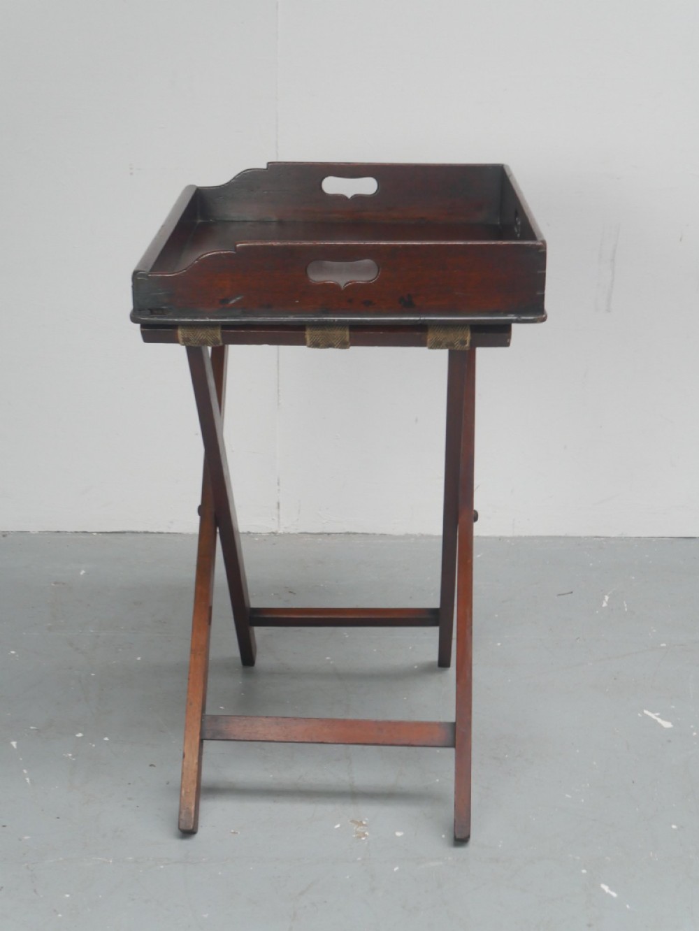 A dark mahogany butlers tray with integrated hand cutout handles resting on a matching folding x-frame stand. View V