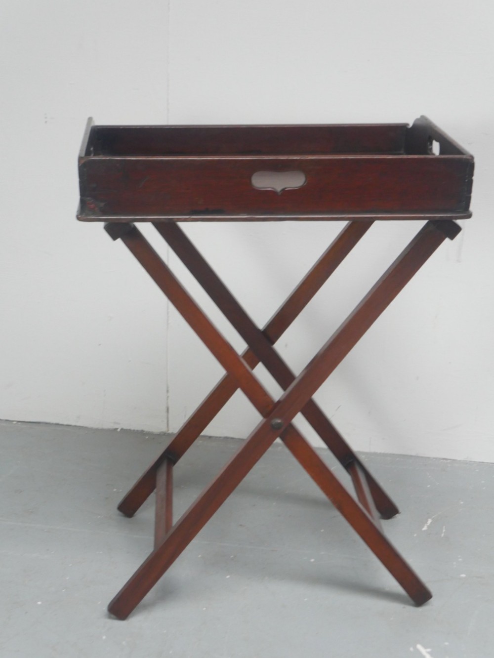 A dark mahogany butlers tray with integrated hand cutout handles resting on a matching folding x-frame stand. View VI