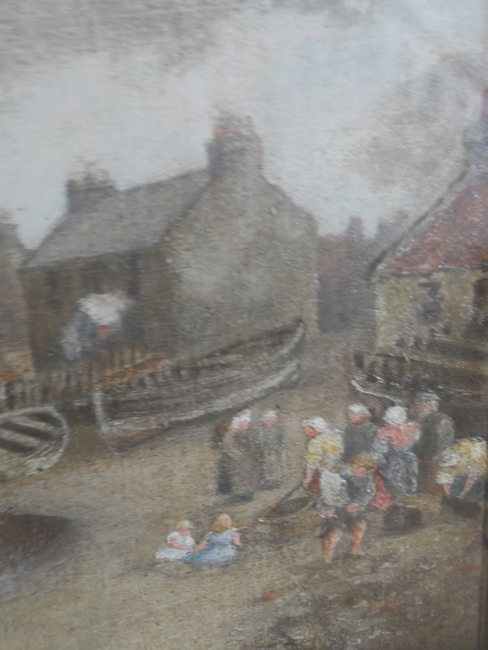 An antique oil painting depicting a coastal village harbour scene with figures along the shore, displayed within an ornate gold swept frame. View V