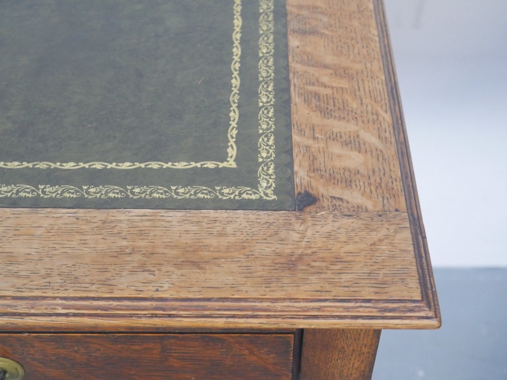 A warm brown oak writing desk with two drawer fronts featuring brass drop handles, resting on four square tapered legs. View IV