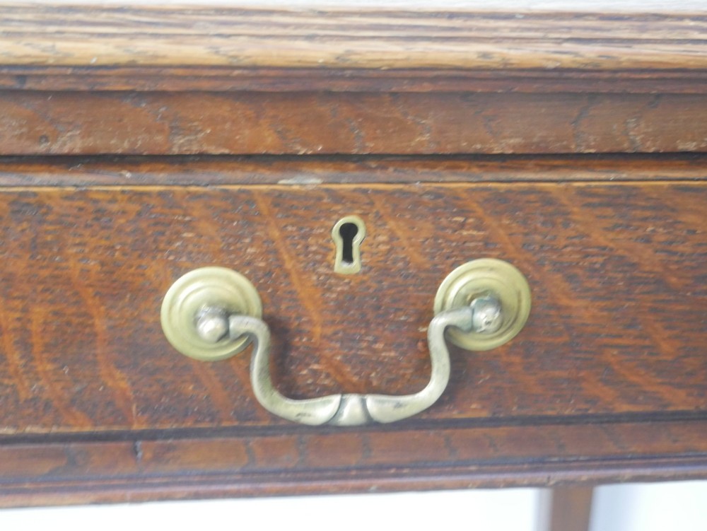 A warm brown oak writing desk with two drawer fronts featuring brass drop handles, resting on four square tapered legs. View VI