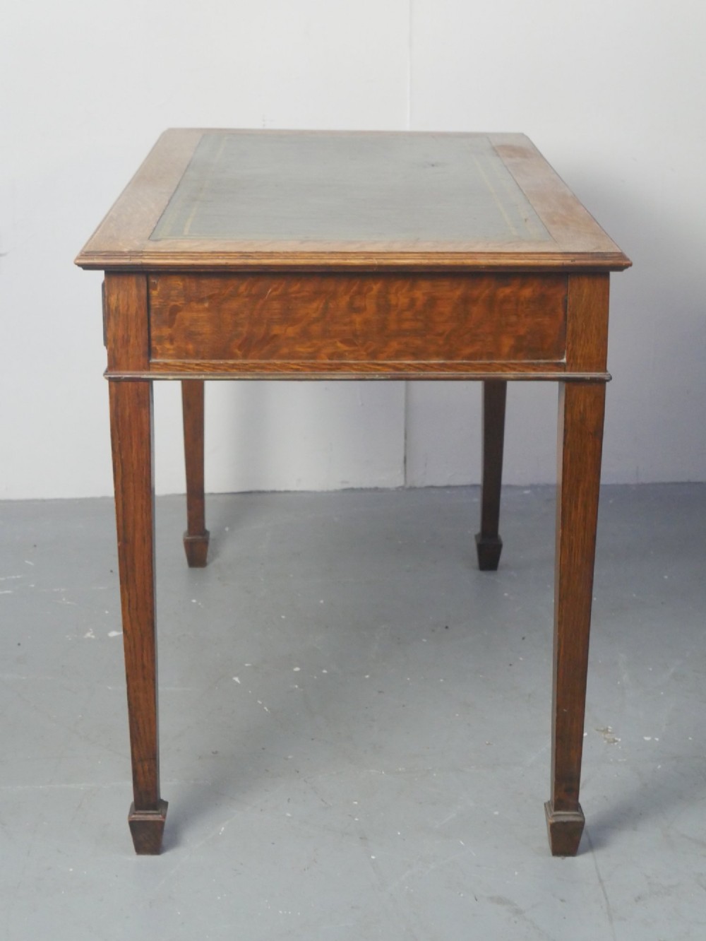 A warm brown oak writing desk with two drawer fronts featuring brass drop handles, resting on four square tapered legs. View VII